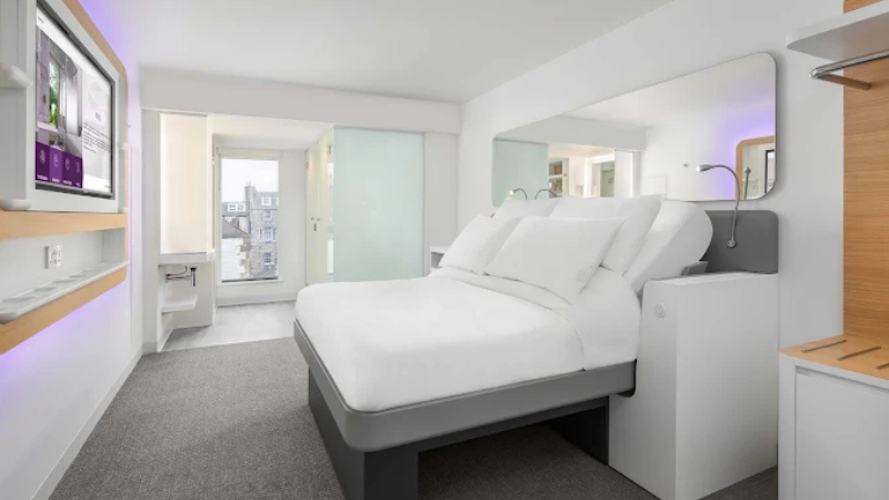 Modernt hotellrum på YOTEL Edinburgh med smart säng, minimalistisk design, stora speglar och ljusa färger.